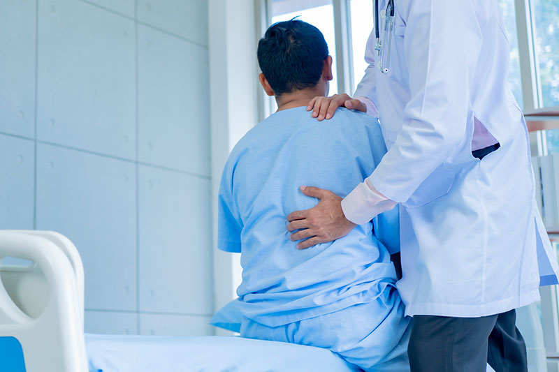 Schmuckbild: ein Arzt untersucht den schmerzenden Rücken eines Patienten, auf einem Krankenhausbett sitzt Schmuckbild: ein Arzt untersucht den schmerzenden Rücken eines Patienten, auf einem Krankenhausbett sitzt