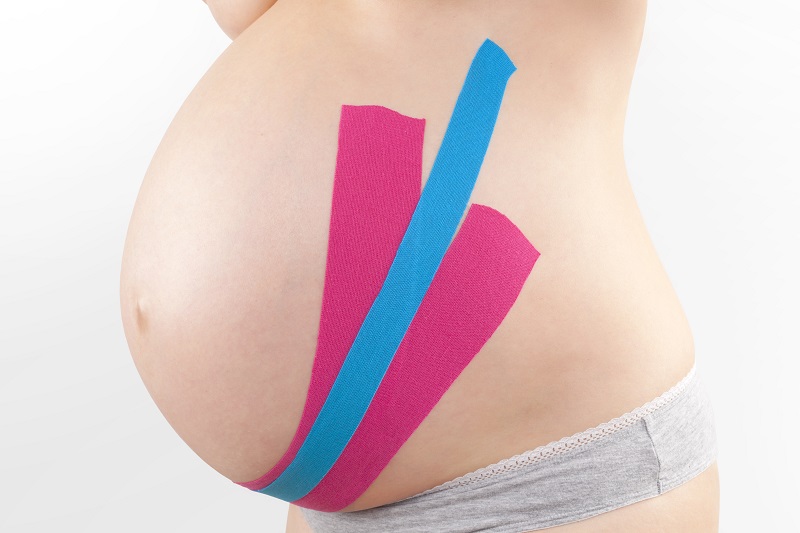 Schmuckbild. Nackter hochschwangerer Bauch, mit Kinesio-Tape in blau und magenta beklebt