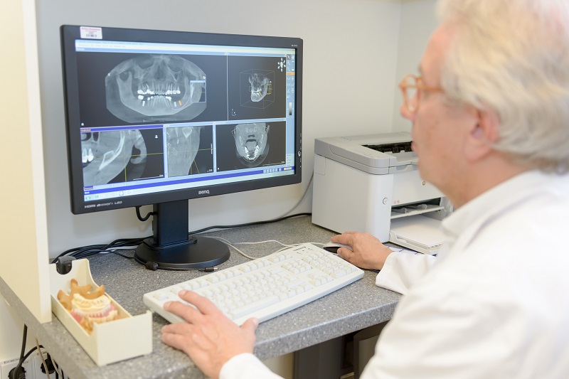 Dr. Köper aus der Praxis für Mund-, Kiefer- und Gesichtschirurgie betrachtet Röntgenbilder der Kiefer am Computerbildschirm
