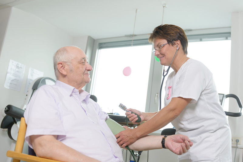 Eine Pflegerin misst den Blutdruck bei einem älteren Patienten