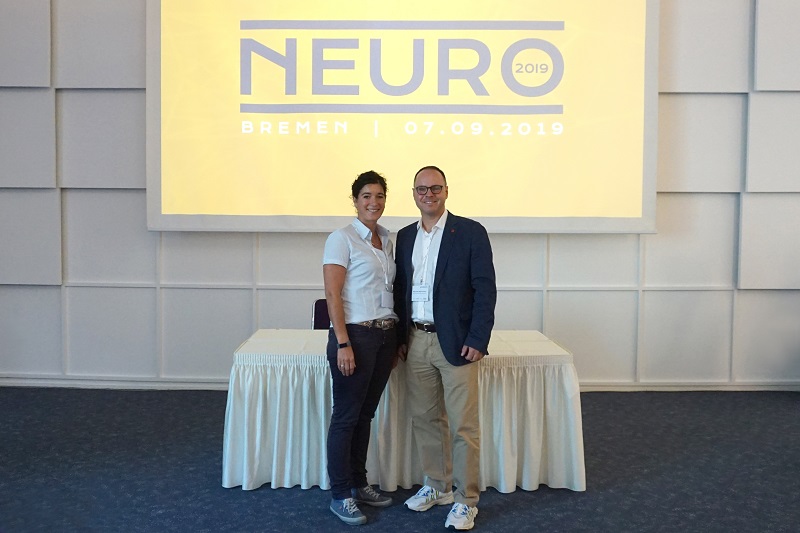 Daniela Lehmhecker und Alexander Müller-Porwoll in den Kongressräumen vor einem Plakat der Neuro 2019 in Bremen Daniela Lehmhecker und Alexander Müller-Porwoll in den Kongressräumen vor einem Plakat der Neuro 2019 in Bremen