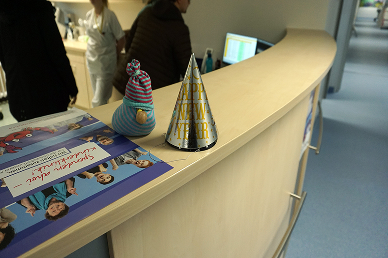 Szenenfoto vom Umzug der Kinderklinik, der Empfangstresen mit einem Neujahrs-Partyhut, einem Stofftier und dem Plakat mit dem Spendenaufruf Szenenfoto vom Umzug der Kinderklinik, der Empfangstresen mit einem Neujahrs-Partyhut, einem Stofftier und dem Plakat mit dem Spendenaufruf