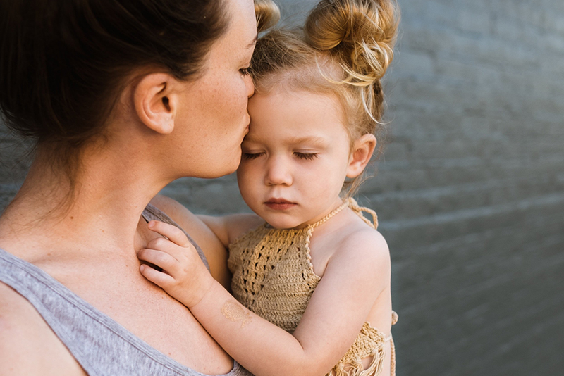 Mutter hält kleine Tochter im Arm und gibt ihr einen Kuss auf die Stirn