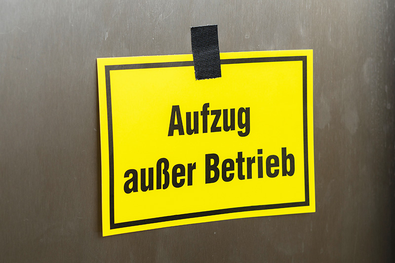 Foto eines gelben Schildes an einer Aufzugtür mit der Aufschrift "Aufzug außer Betrieb"
